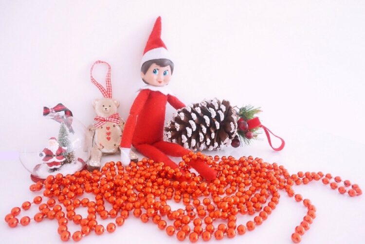 Lazy, easy, Elf on the Shelf ideas | Image shows an elf on the shelf surrounded by Christmas decorations.