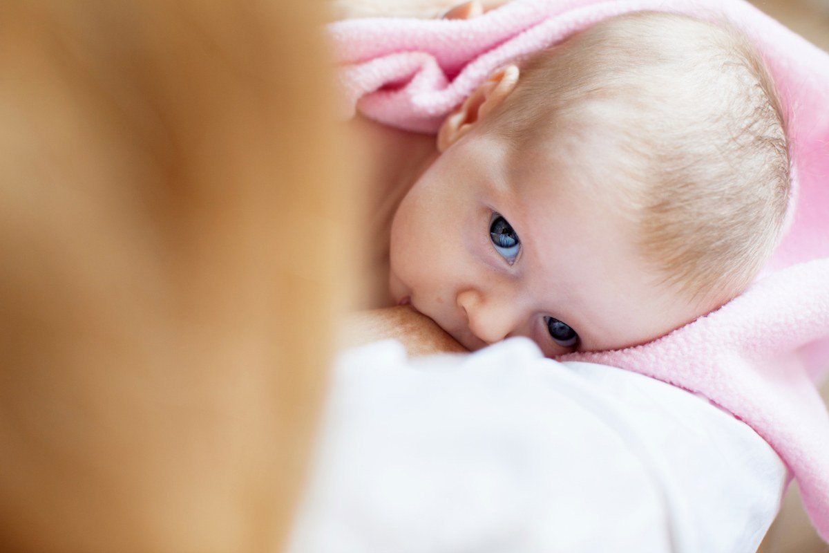 Image shows a nursing infant wrapped in a pink blanket.