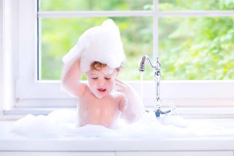 How to wash toddler hair | Image shows a toddler in a kitchen sink rubbing bubbles into her hair.