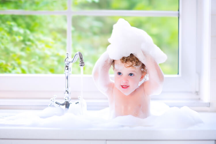 Washing toddler hair | Image shows a toddler in a kitchen sink rubbing bubbles into her hair.
