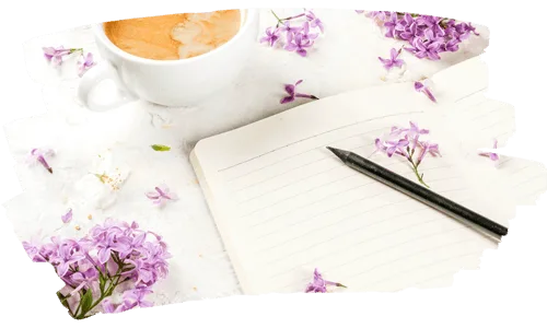 Journal prompts | A cup of coffee beside an open journal with scattered purple flowers on a white desk.