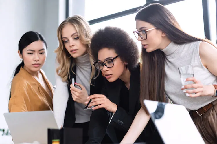 Group names for girls | Image shows four women in an office looking at a laptop screen.