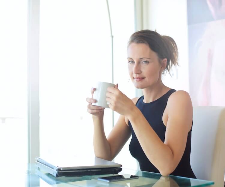 Informal female headshot of a woman sitting at her desk holding a mug.