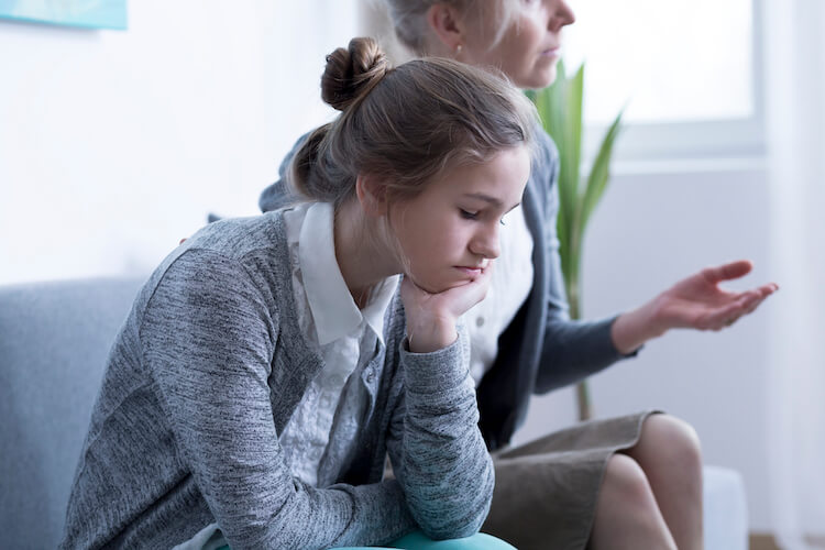 Girl looking sad while she sits in a therapist's office with her mother.