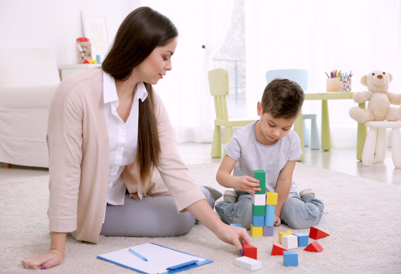 Play therapy activities for anxiety | Therapist sitting beside a child who is playing with bricks on the floor.