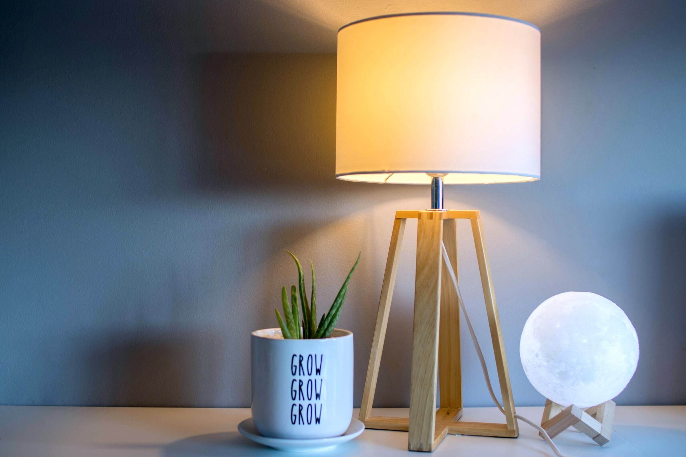 A lamp on three wooden legs with a globe style lamp on one side and a small plant pot on the other.