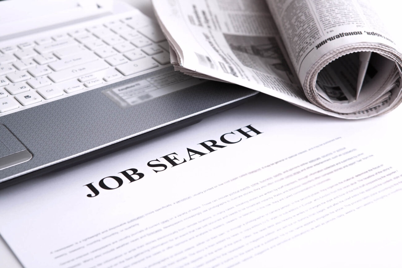 Flatlay for job search, showing a laptop and a rolled up newspaper.