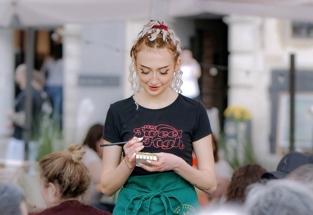 A teenage waitress wearing a green apron and writing an order on a pad.